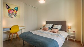 A bedroom with a bed, a desk, a chair, and a nightstand with a lamp. - Cosy apartment with large balcony and private parking (Lorient)