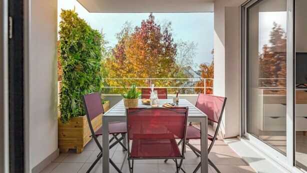 A balcony with a table and chairs, a potted plant, and a view of trees. - Cosy apartment with large balcony and private parking (Lorient)