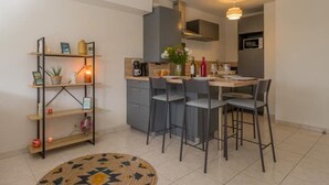 A modern kitchen with grey cabinets, a dining area with four chairs, and a small shelf unit with decorative items. - Cosy apartment with large balcony and private parking (Lorient)