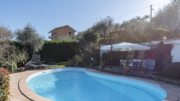 A swimming pool with a stone border, a patio area with outdoor furniture, and a building in the background. - Villa Renetta (San Massimo)