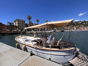 Un barco amarrado en un muelle con una zona de estar cubierta, un timón y una cuerda atada a un pilón.