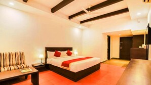A hotel room with a bed, a sofa, a table, and a TV. - Reva Resorts & Holiday Homes (Puttur)