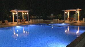 A swimming pool with two covered seating areas, each with a table and chairs. - Reva Resorts & Holiday Homes (Puttur)