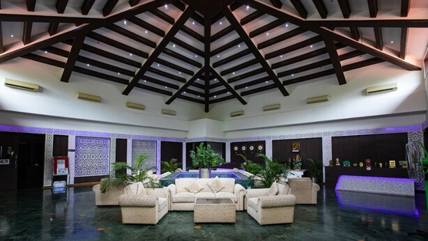 A spacious lobby with a high ceiling, a central seating area, and decorative wall panels. - Reva Resorts & Holiday Homes (Puttur)