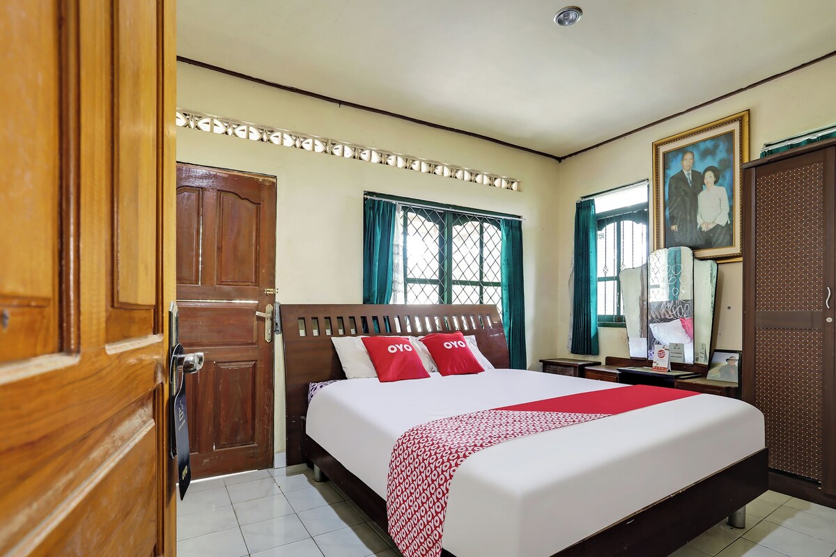 A hotel room with a bed, wooden wardrobe, a desk, and a window with curtains.