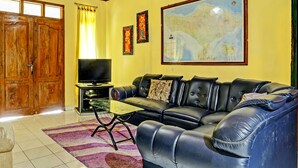 Un salón con un sofá de cuero negro, una mesa de centro de vidrio, un televisor de pantalla plana, un mapa grande en la pared y una puerta de madera.