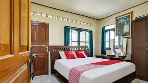 Habitación de hotel con una cama grande, un armario de madera y una pequeña mesa con lámpara.