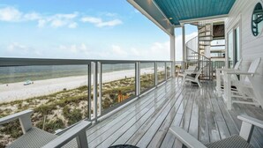 Terraza de madera con barandilla de vidrio con vista a la playa.