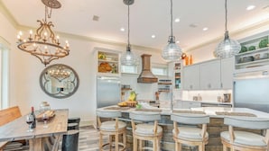 Cocina moderna con una isla central, taburetes de bar, una araña y luces colgantes.