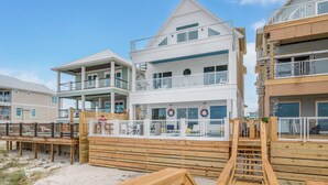 Un edificio de varios pisos frente a la playa, con balcones, una terraza de madera y un puesto de salvavidas.
