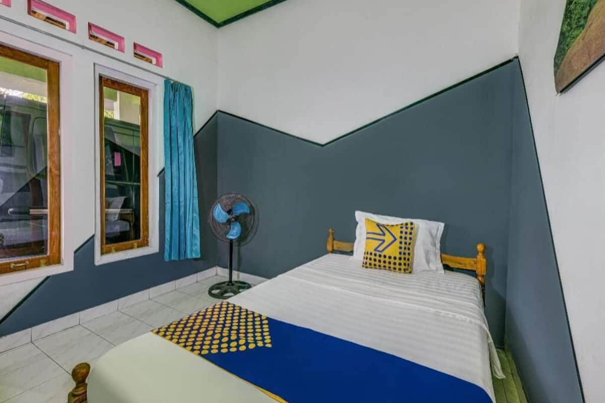 Une chambre à coucher avec un lit, un ventilateur, une fenêtre avec des rideaux et une porte.