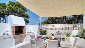 Une terrasse extérieure avec un barbecue, des meubles blancs et des plantes en pot.