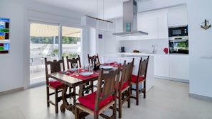 Une cuisine moderne avec des meubles blancs, un four encastré et un coin repas doté de chaises en bois et de coussins rouges.