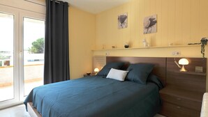 A bedroom with a bed, a nightstand, a lamp, a window with curtains, and wall art. - GERKENS: Holiday home with communal pool in l'Escala (L'Escala)