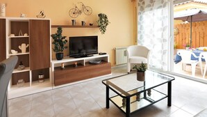 A living room with a TV, a glass coffee table, a white chair, and a wooden cabinet. - GERKENS: Holiday home with communal pool in l'Escala (L'Escala)