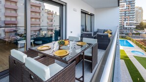 Een balkon met rieten meubels, een eettafel gedekt met borden en glazen, en uitzicht op een woongebied met gebouwen.