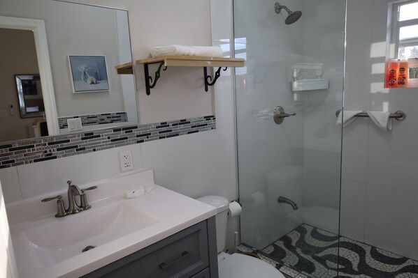 Une salle de bain moderne avec un lavabo blanc, une douche en verre et un mur recouvert de carreaux.