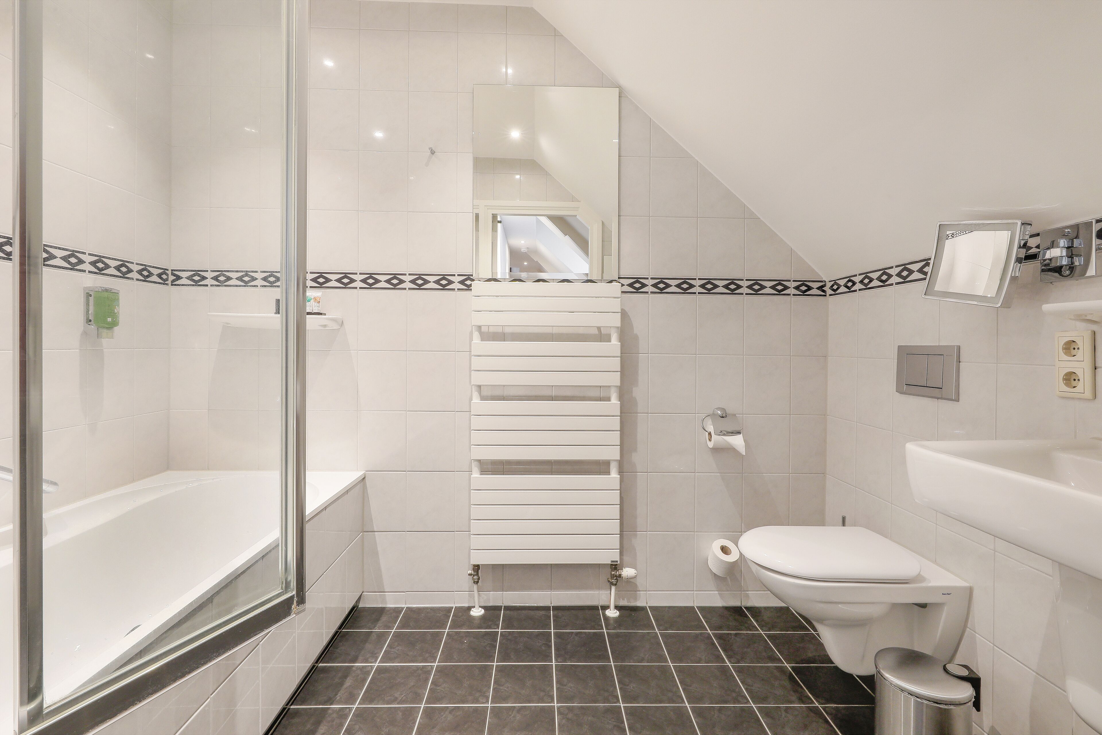 A modern bathroom with a glass shower enclosure, a white bathtub, a toilet, and a sink.