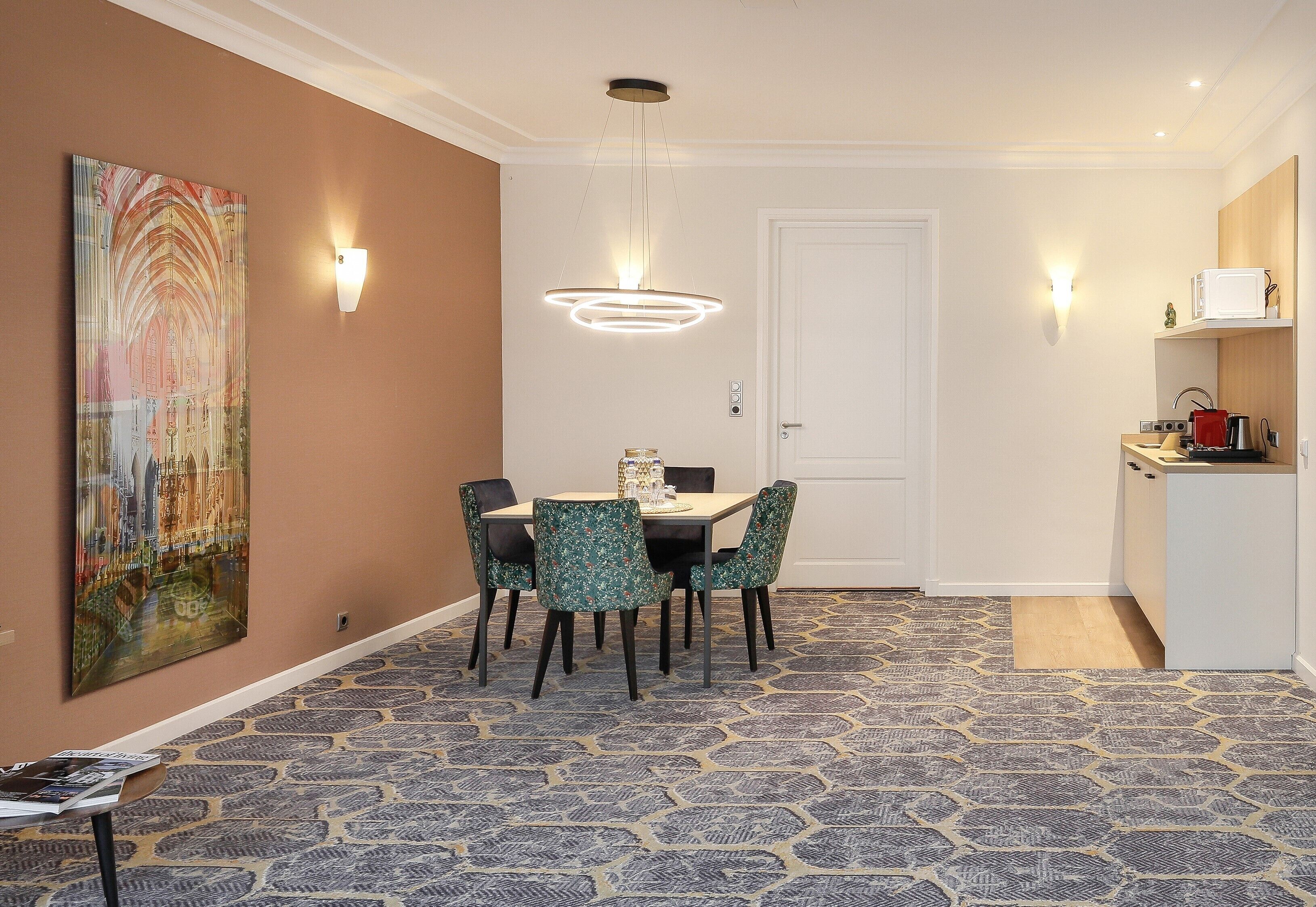 Un comedor con una mesa, sillas, una lámpara en la pared y una puerta al fondo.