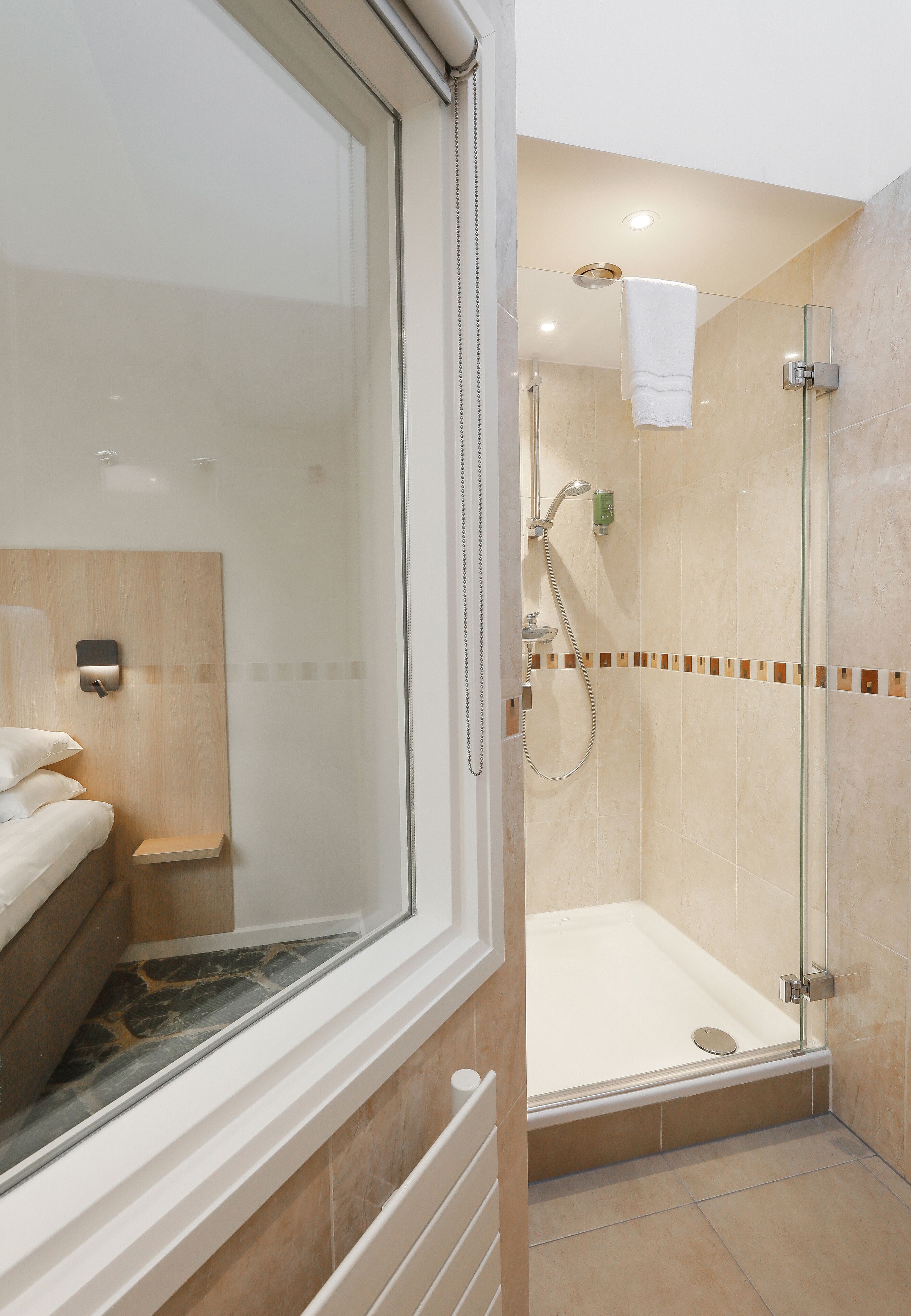 A modern bathroom with a glass shower enclosure, a visible towel rack, and a built-in bench.