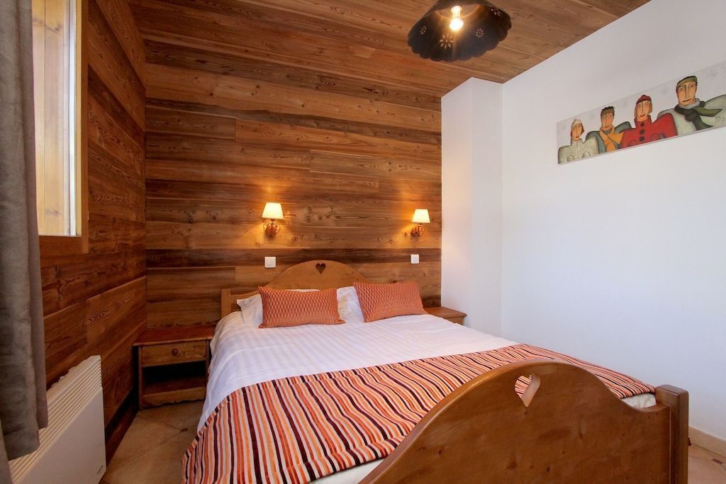 Une chambre aux murs lambrés, avec un lit, deux lampes fixées au mur et un tableau accroché au mur.