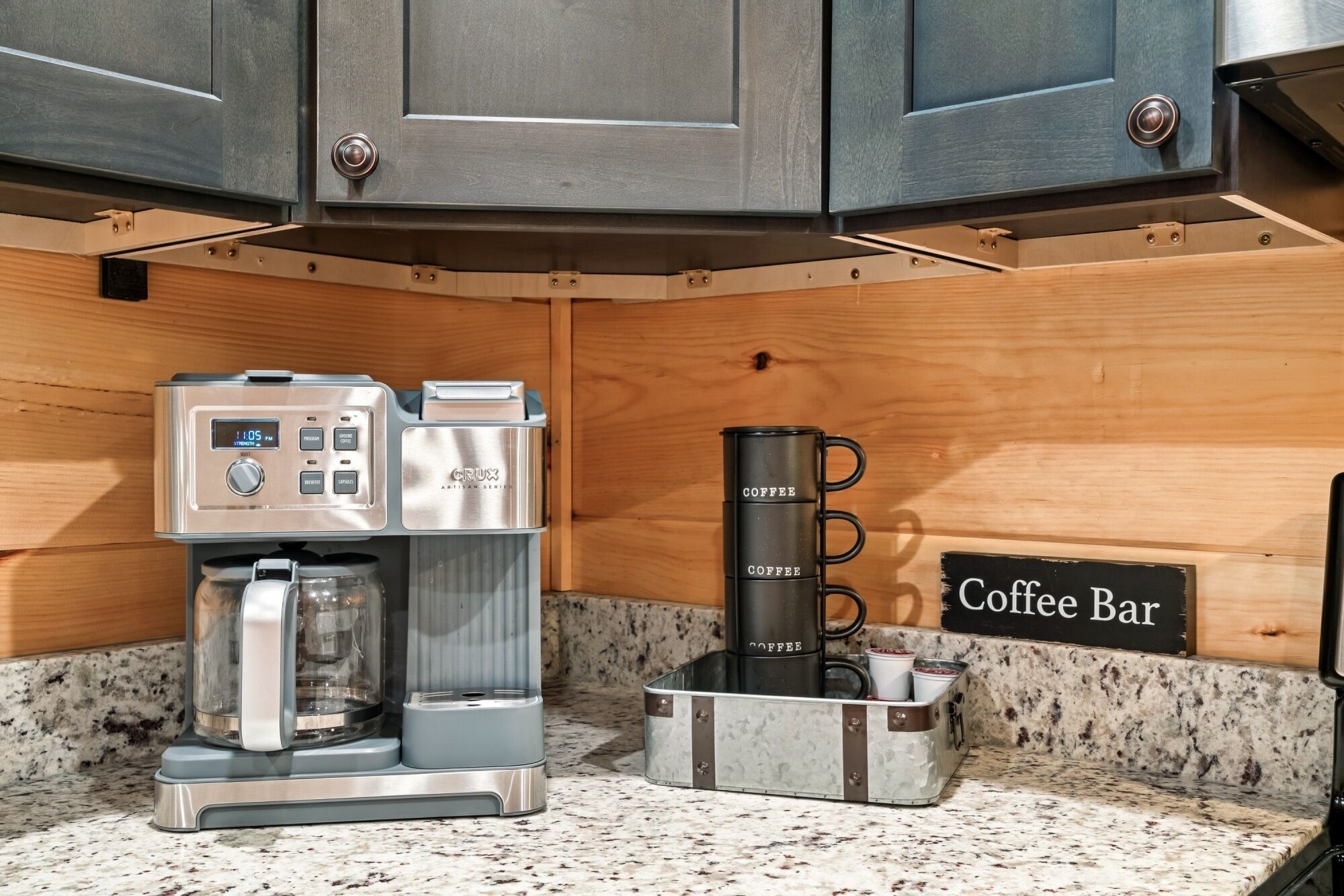 A coffee station with a coffee maker, a coffee dispenser, and a coffee mug on a granite countertop.