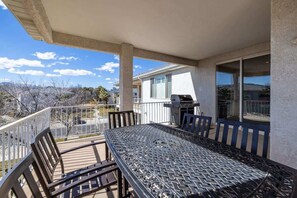 A balcony with a metal table and chairs, a barbecue grill, and a view of a residential area.