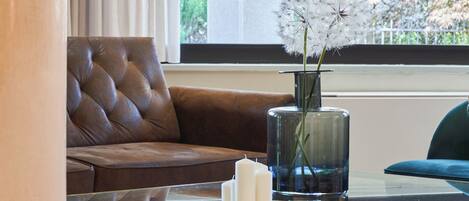 A modern living room with a brown leather sofa, a glass coffee table with gold legs, and a vase with white flowers.