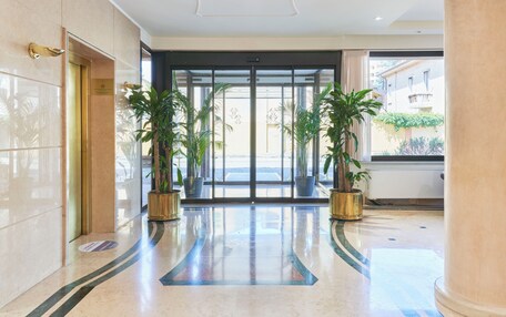 A hotel lobby with a marble floor, a glass elevator, and potted plants.