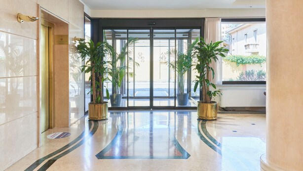 Un vestíbulo de hotel con piso de mármol, un ascensor de vidrio y plantas en macetas.