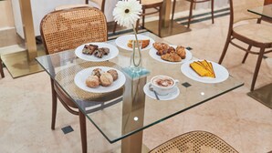 Una mesa con cubierta de vidrio, platos de pasteles, una taza de café y una flor blanca.