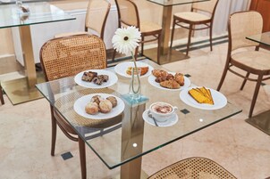 Uma mesa com tampo de vidro, pratos com doces, uma xícara de café e uma flor branca.