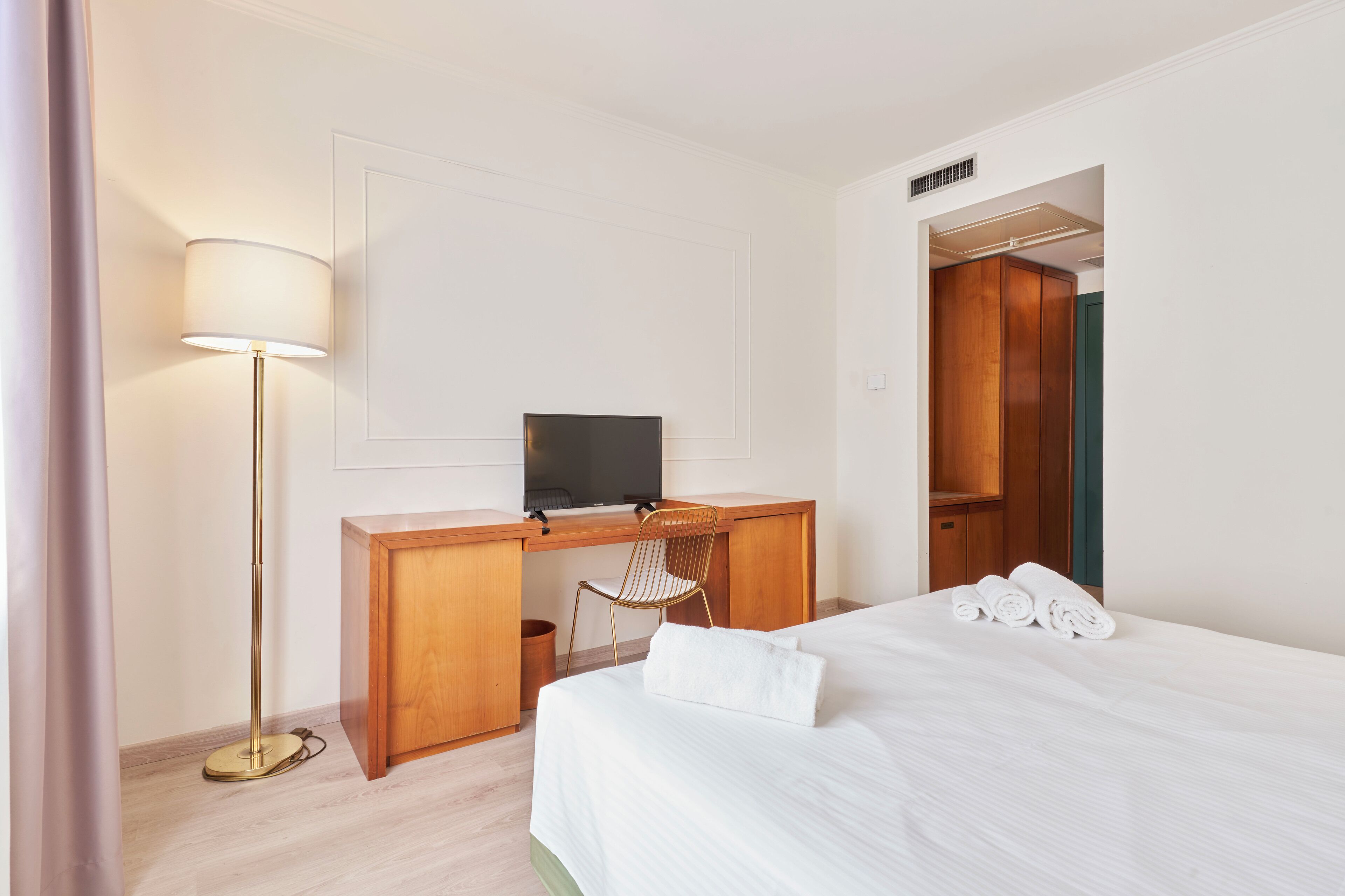 Habitació d'hotel amb llit, escriptori amb ordinador, cadira i làmpada.