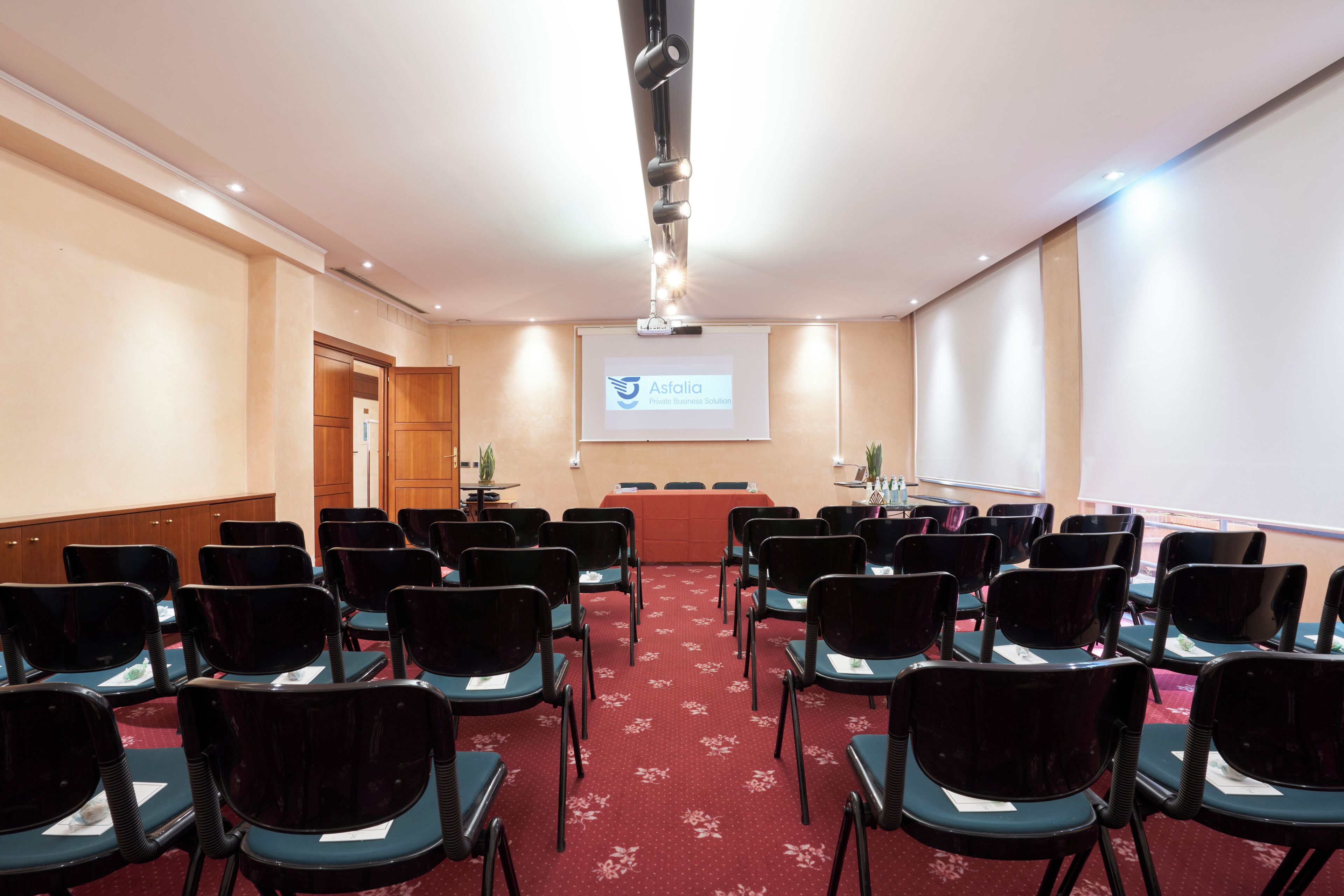 Un salón de conferencias con filas de sillas, una pantalla de proyección y un atril.