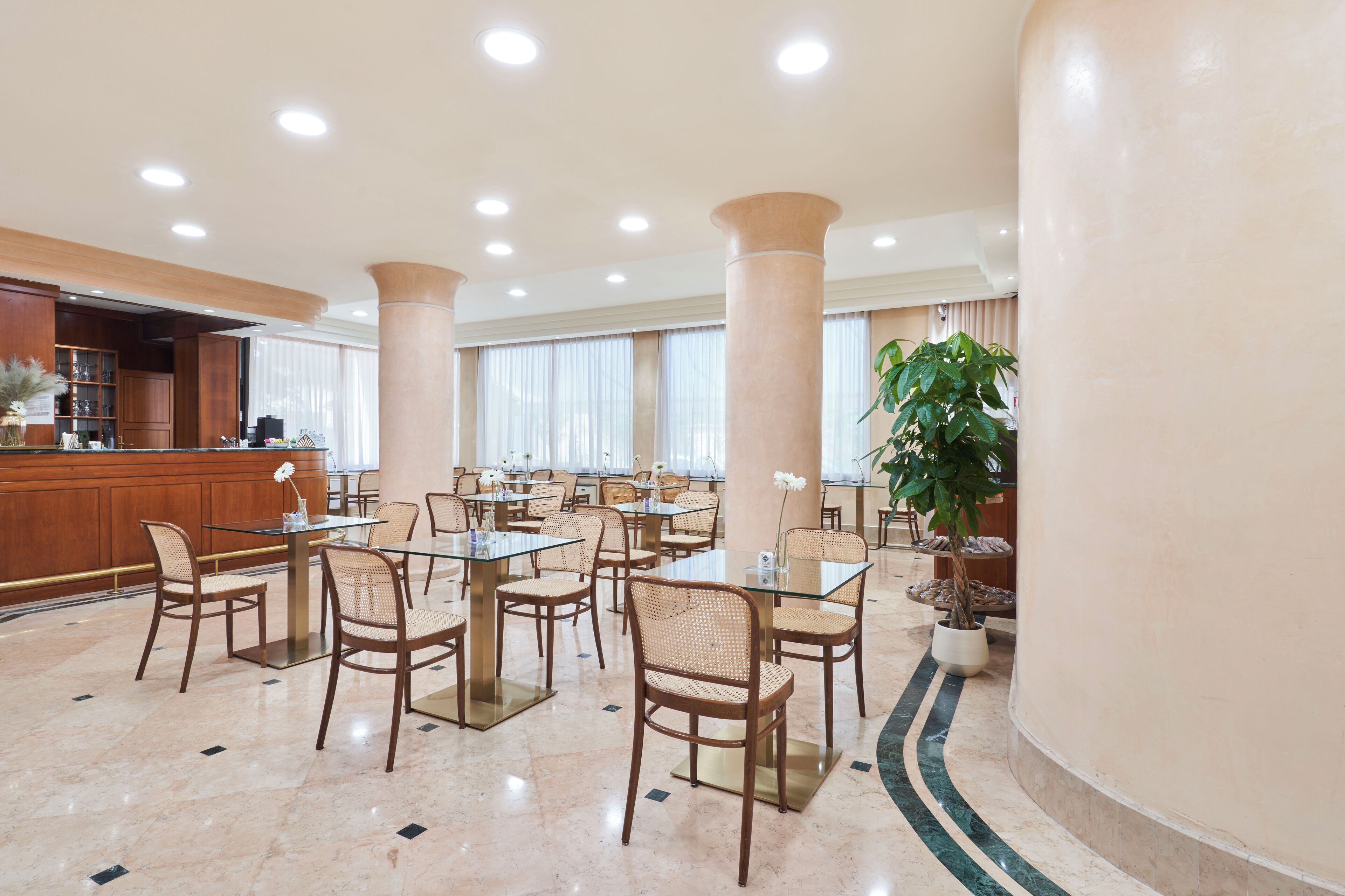 Un hall d’hôtel spacieux, doté de nombreuses tables et chaises, d’un comptoir de réception et de grandes colonnes.