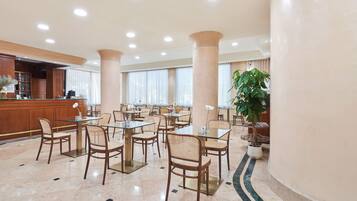 Un hall d’hôtel spacieux, doté de nombreuses tables et chaises, d’un comptoir de réception et de grandes colonnes.