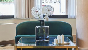 Un salón moderno con un sofá verde, una mesa de centro de vidrio y un jarrón con flores blancas.
