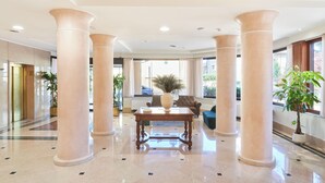 Un vestíbulo espacioso con amplias columnas, una mesa central y plantas en macetas.
