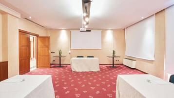 A conference room with a red carpet, a white projection screen, two tables with white tablecloths, and a wooden door.