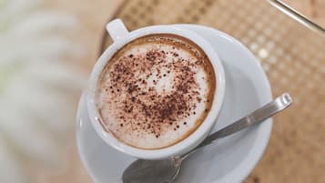 Una taza de café con una cuchara sobre un plato, colocada sobre una mesa de vidrio, con una silla de mimbre al fondo.