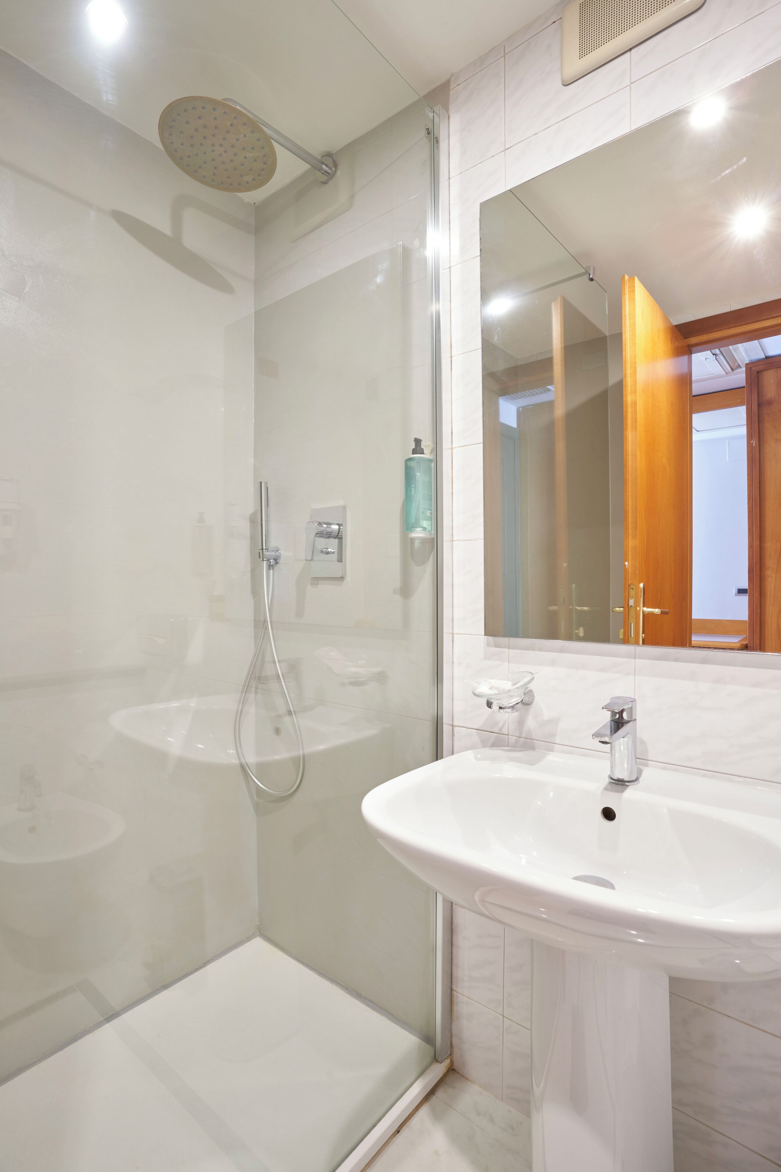 A modern bathroom with a glass-enclosed shower, a pedestal sink, and a large mirror.