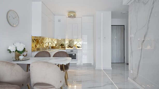 Une cuisine moderne avec des meubles blancs, un pare-feu en marbre et un coin repas comprenant une table et des chaises blanches.