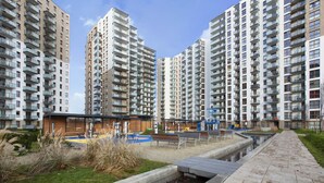 Un quartier résidentiel moderne avec de grands immeubles d’appartements, une promenade dallée et un petit élément décoratif aquatique.