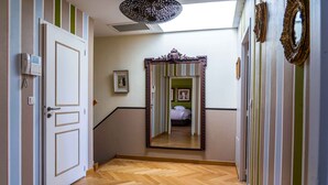 A hallway with a wooden herringbone floor, a white door with a keyhole, a wall-mounted intercom, and a mirror reflecting a bed and a green-striped wall. - Voltaire - Magnificent 4-bedroom duplex in Triangle d'Or (Bordeaux)