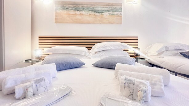 A hotel room with a bed, two bedside tables, a wall-mounted air conditioner, and a painting of a beach scene. - Casa Rosa Tre, Rapallo, 1b/1b with private parking and garden (San Massimo)