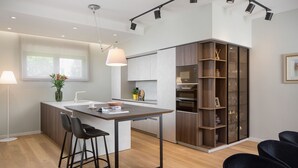 A modern kitchen with a central island, bar stools, a built-in oven, and a wooden cabinet with glass doors.