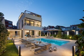 Ett modernt hus i två våningar med en swimmingpool, utomhusmöbler och en väl upplyst uteplats.
