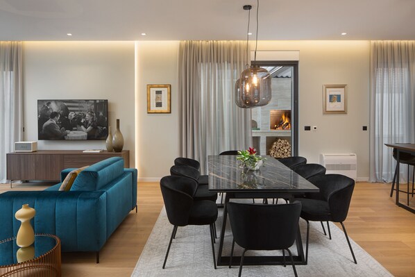 Una sala de estar moderna con un sofá azul, sillas negras, una mesa de comedor con superficie de vidrio y un televisor de pantalla plana grande.