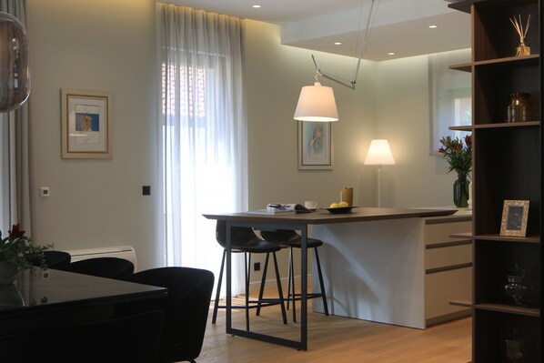 Et moderne køkken med spiseplads, med en køkkenø, barstole, hængende lamper og et bogreol.