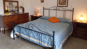 Un dormitorio con cama, cómoda, mesita de noche, lámpara y un cuadro en la pared.